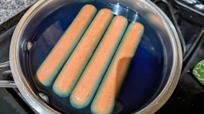 Four hot dogs floating in Gatorade in saucepan.