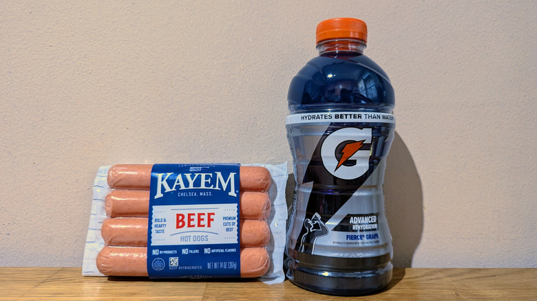 Package of hot dogs next to grape-flavored Gatorade on counter.