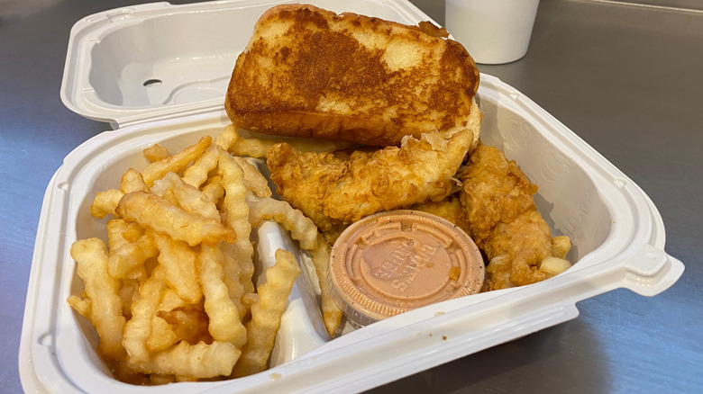 Takeout container of crinkle fries, chicken tenders, and toasted bread from Raising Cane's