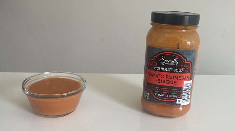 A bowl of tomato bisque next to the jar of it