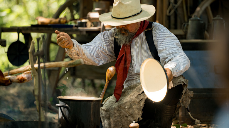 Cowboy leaning over a pot and cooking