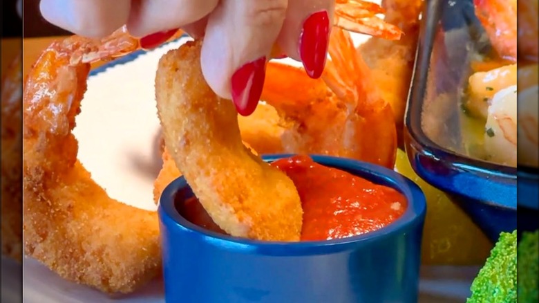 Person dipping shrimp into cocktail sauce