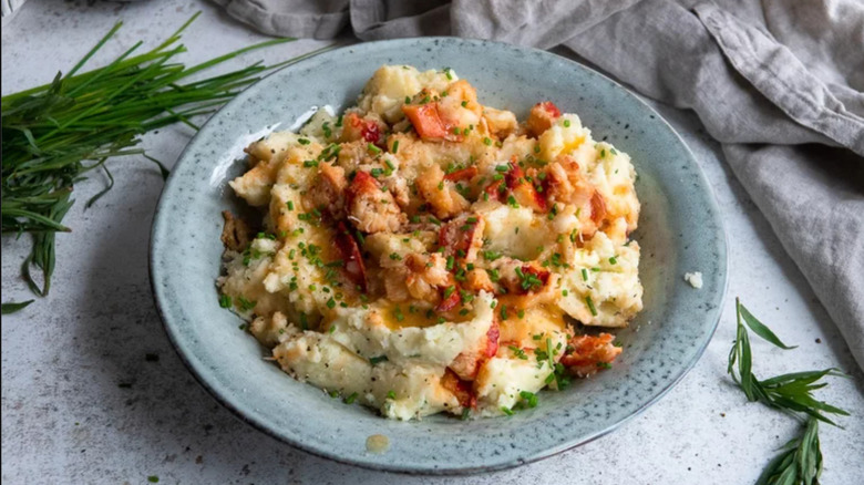 A bowl of mashed potato with fresh herbs and lobster