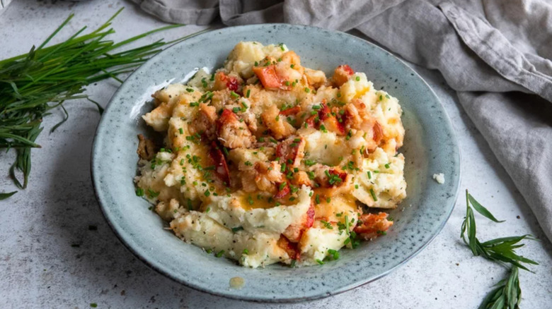 A bowl of mashed potato with fresh herbs and lobster