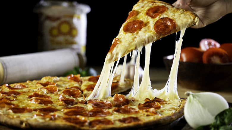 A person pulling an incredibly cheesy slice of pizza up from the whole pie