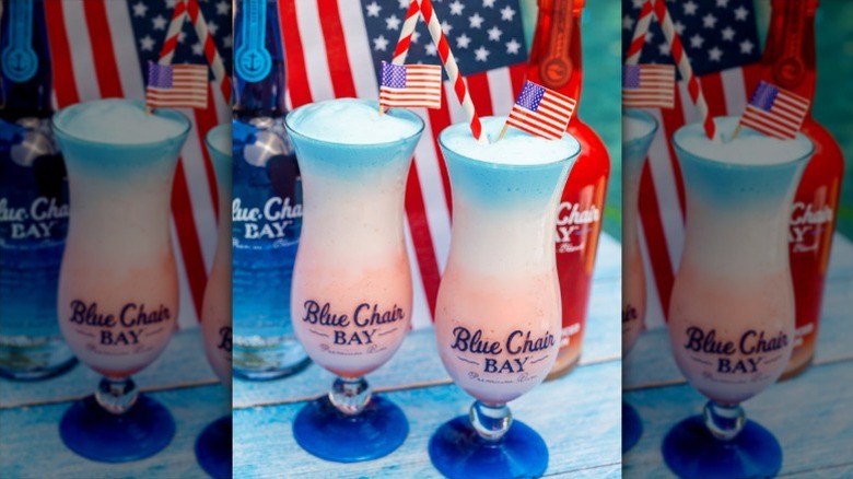 Two red, white, and blue layered frozen drinks garnished with paper flags in hurricane glasses with the Blue Chair Bay Rum logo