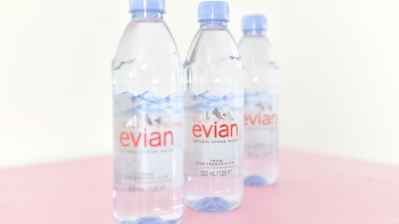 Bottles of Evian water posed in a row on a pastel pink surface.