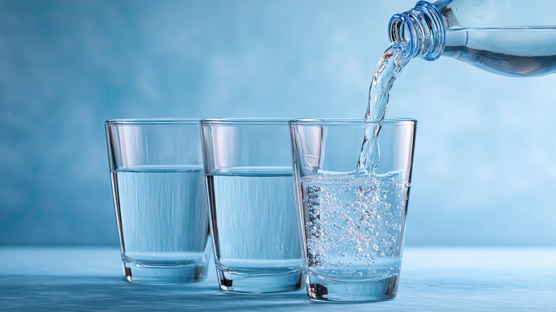 Water getting poured into three glass cups on a pale sky blue background.