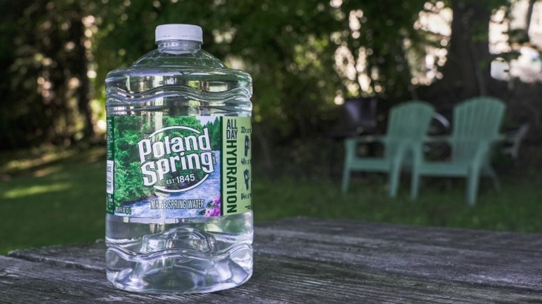 A plastic jug of Poland Spring water on a wooden table with two deck chairs behind it.