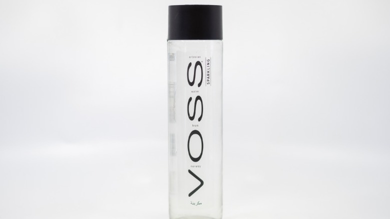 A bottle of Voss water on a grey background.