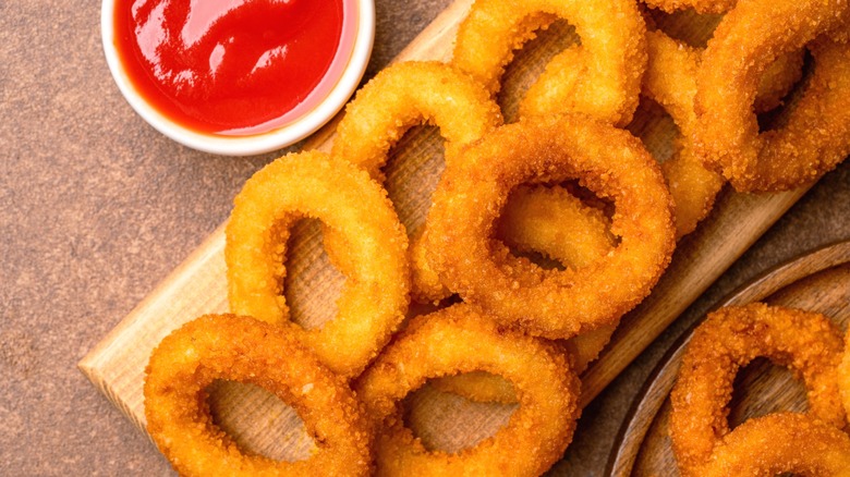 Fried onion rings on a board with ketchup.