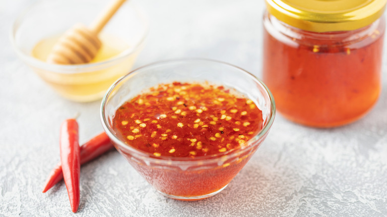 Hot honey in a jar with red chili pepper flakes with a honey comb dipper and red peppers in the background