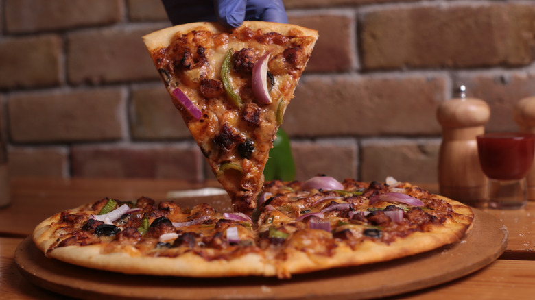 A chicken strip pizza with someone holding up a piece