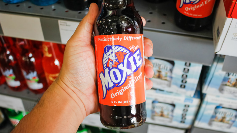 Hand holding a bottle of Moxie in a store