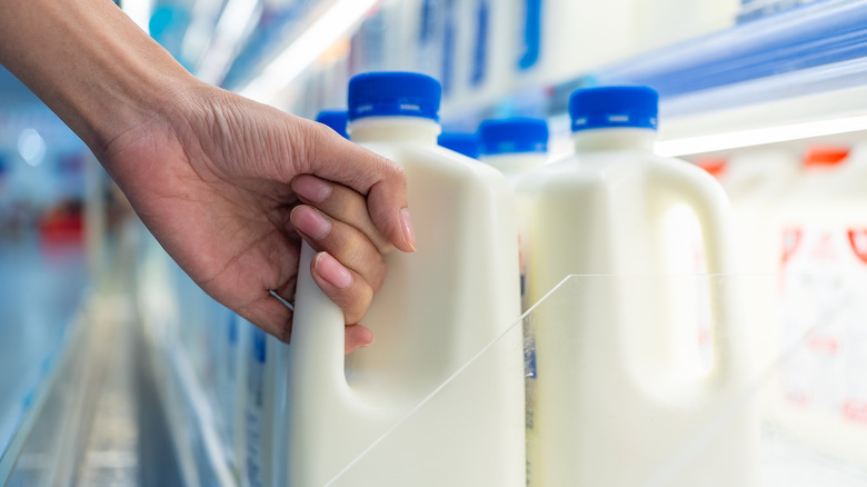 A hand grabs a carton of milk out of a grocery store cooler