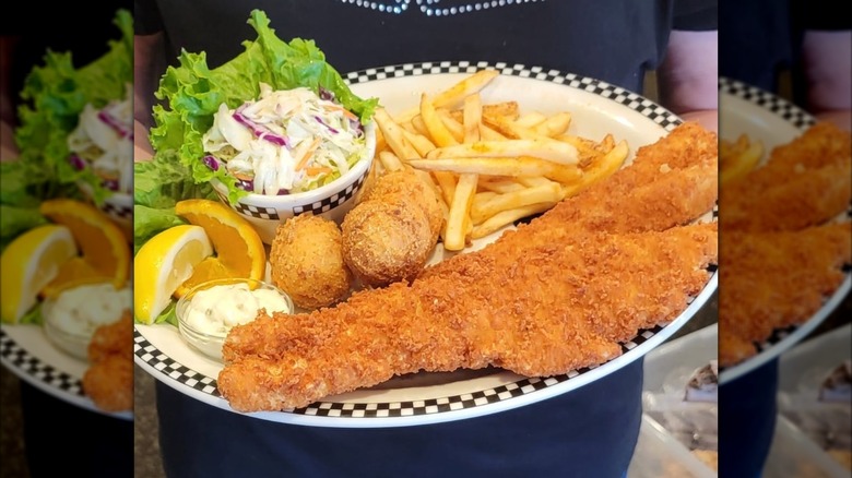 A Black Bear Diner server holding a platter of fried fish, hushpuppies, lemon wedges, tarter sauce, and coleslaw