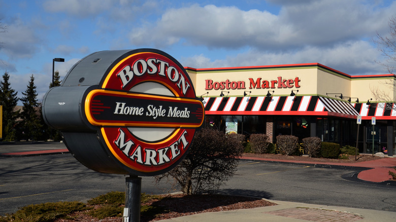 A Boston Market sign which reads "Boston Market Home Style Meals" is shown in the foreground of the Canton location of Boston Market, which has red, white, and black striped awning