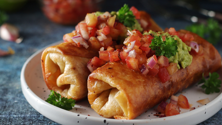 two flour tortilla chimichangas topped with pico de gallo, guacamole, and fresh herbs