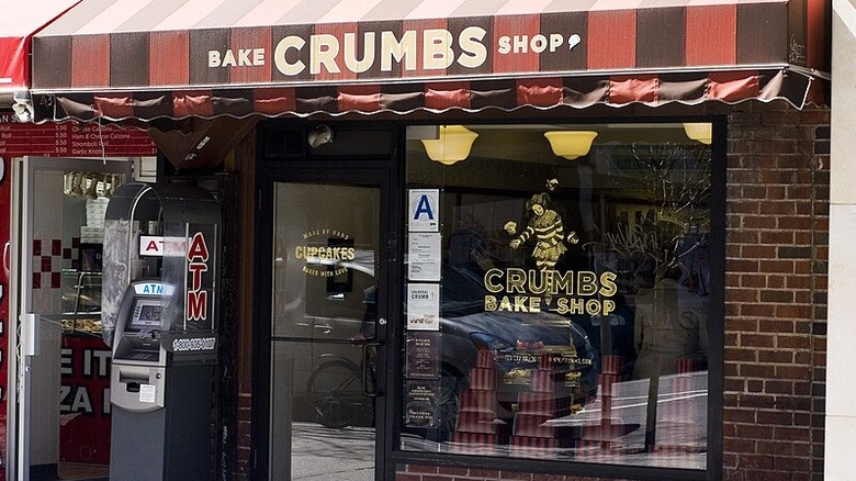 glass front refrigerated case full of shelves of decadently decorated cupcakes with Crumbs labels listing flavors and prices