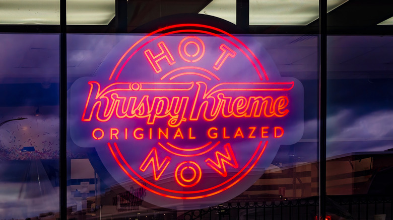 a red neon sign in a restaurant window that reads Krispy Kreme original glazed, Hot Now