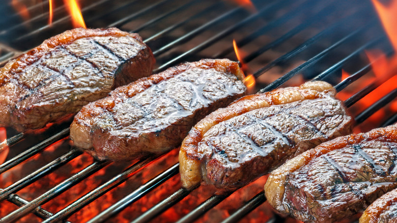 four steaks with a large stripe of fat and charr marks cooking over a grill flame