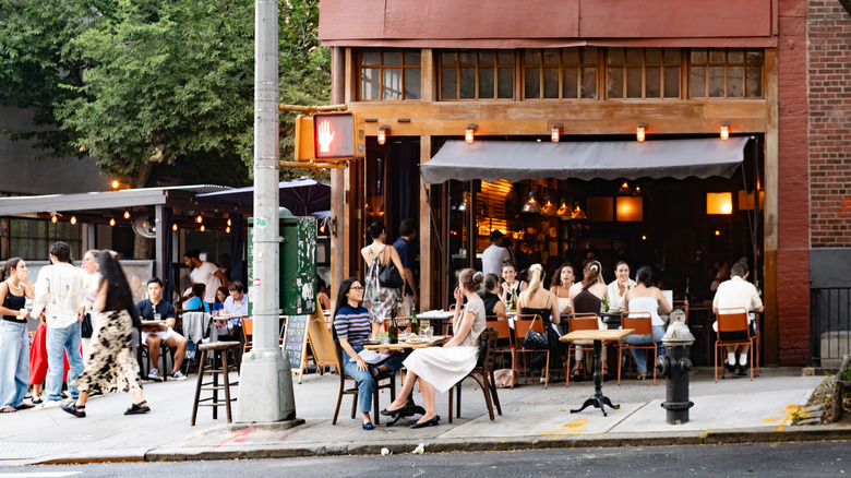 On a summer day many people sit and dine outdoors at a sidewalk cafe in Soho, NYC.