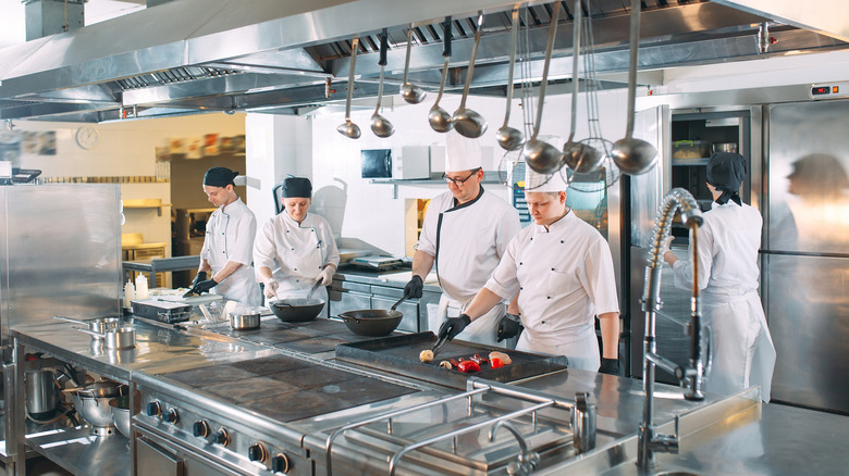 Five chefs wearing uniforms posing in a kitchen