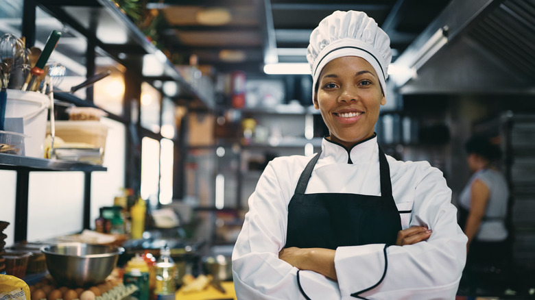 Happy woman standing with arms crossed while working as chef in a restaurant
