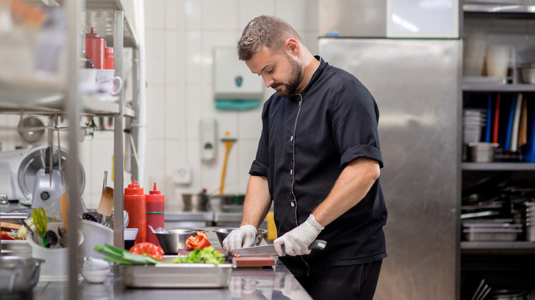 Professional chef in uniform cutting fresh vegetables in kitchen