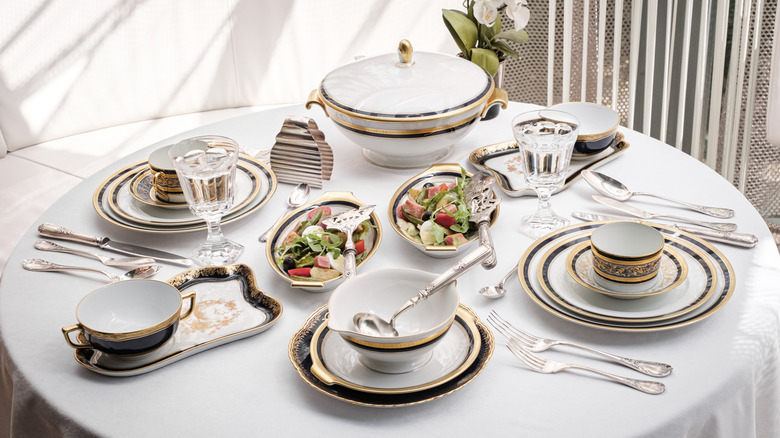 A antique looking table setting on a round dining table with a white table cloth