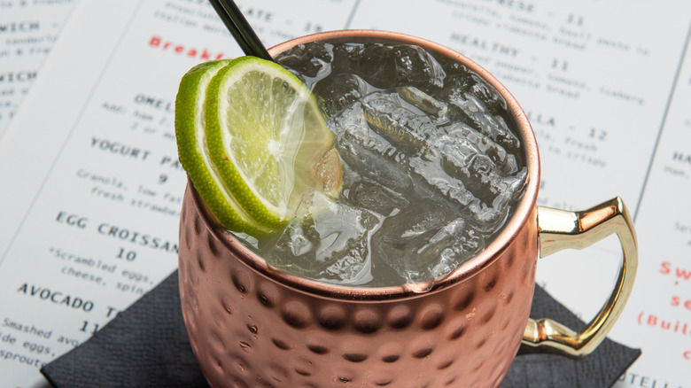 A closeup top-down photo of a Moscow mule in a metal glass, rests on a square black napkin on a menu
