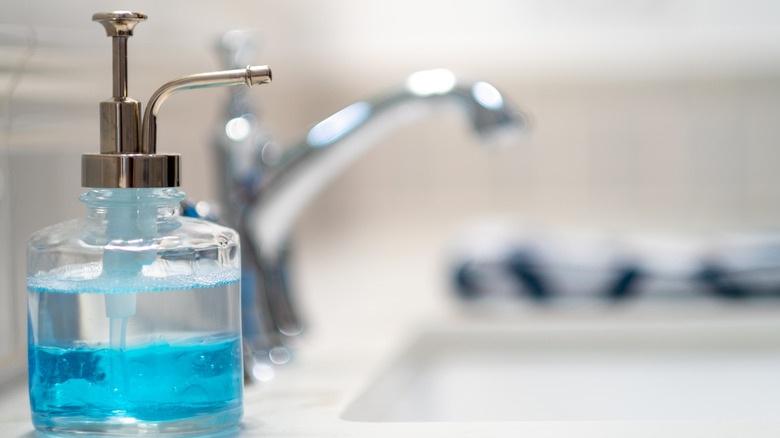 A fancy looking soap dispenser with blue soap on the ledge of a sink in the bathroom