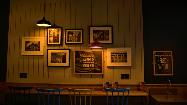 Three barstools against a bar top with several pictures of architecture hanging on the wall and a single light shining over the bar