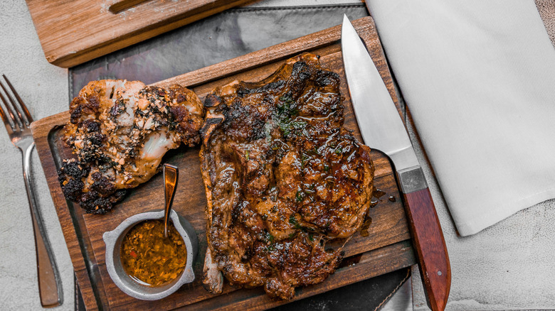 A platter of steak and chicken served on a wooden cutting board, with a steak knife and fork on either side