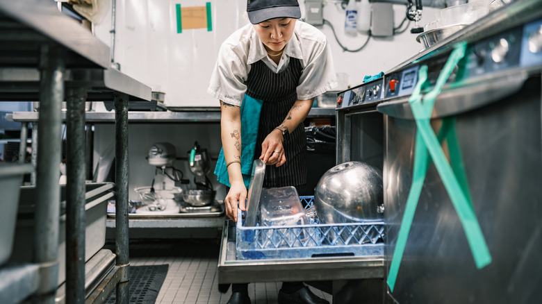 A restaurant worker loads a dishwasher.