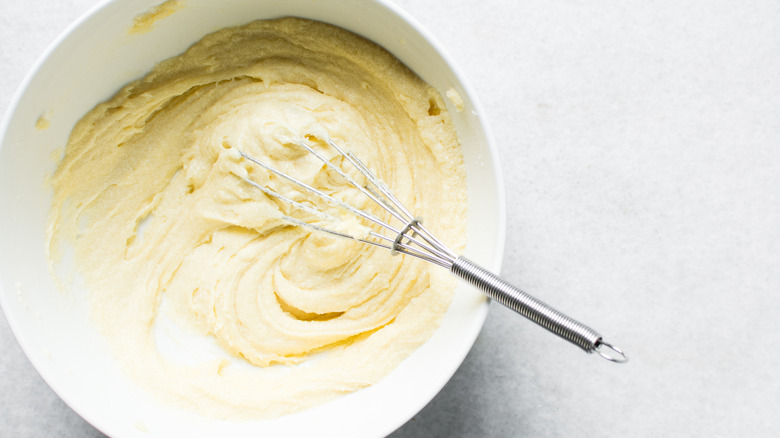 A top-down view of butter being mixed into sugar in a white bowl