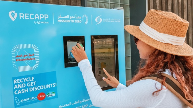 A young woman in a hat using a reverse vending machine.