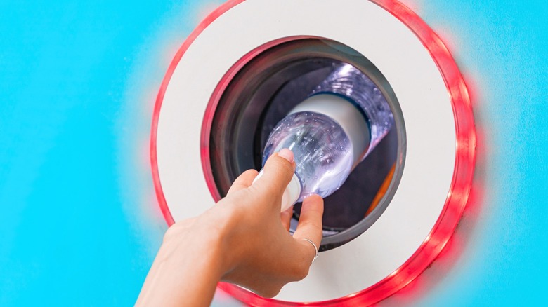 A person feeding a plastic water bottle into a reverse vending machine.
