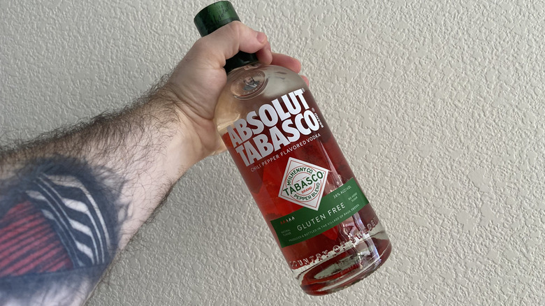 arm holding Absolut Tabasco bottle against a white wall