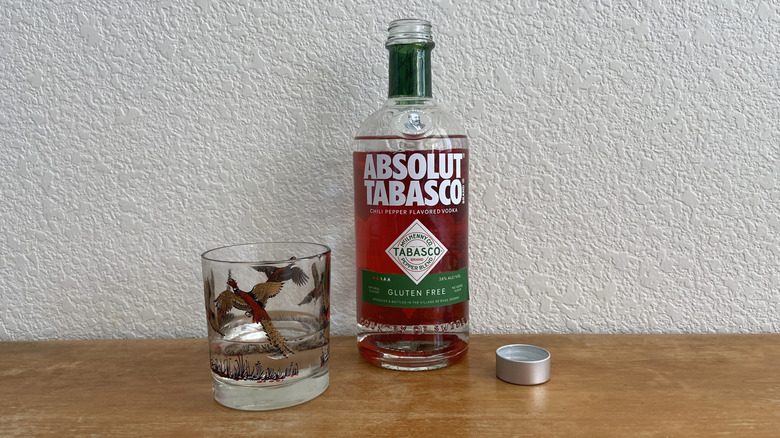 open Absolut Tabasco bottle beside a filled glass and its cap
