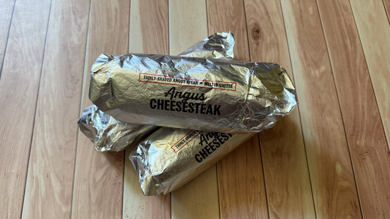 Angus cheesesteak sandwiches from Arby's wrapped in branded foil wrappers on table
