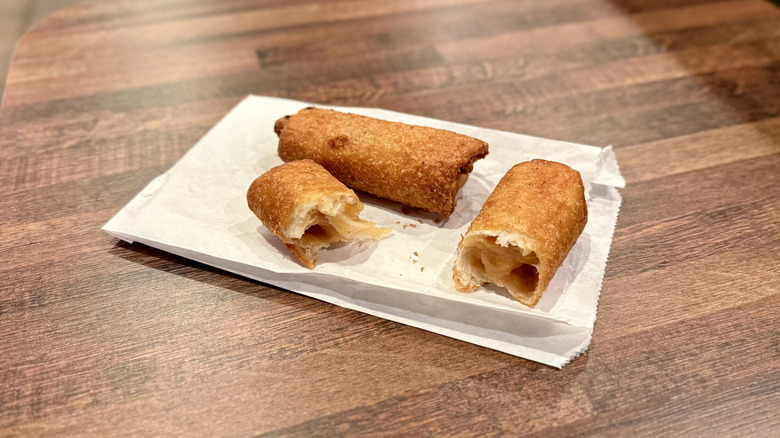 One peach cobbler roll split open and another whole roll on paper bag on wooden table