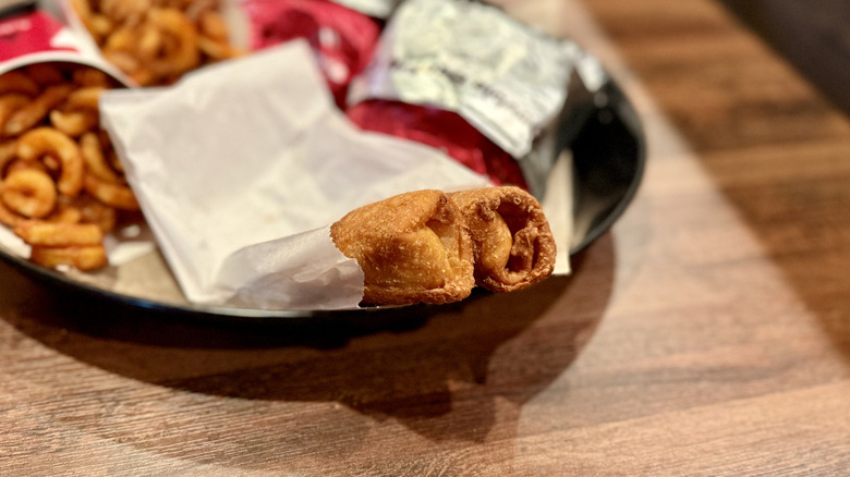 Two peach cobbler rolls in paper bag on a tray with orders of curly fries and wrapped hamburgers on wooden table