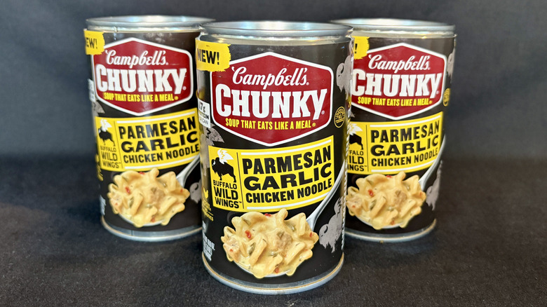 Three cans of Campbell's Buffalo Wild Wings Chunky Parmesan Garlic Chicken Noodle soup on black background