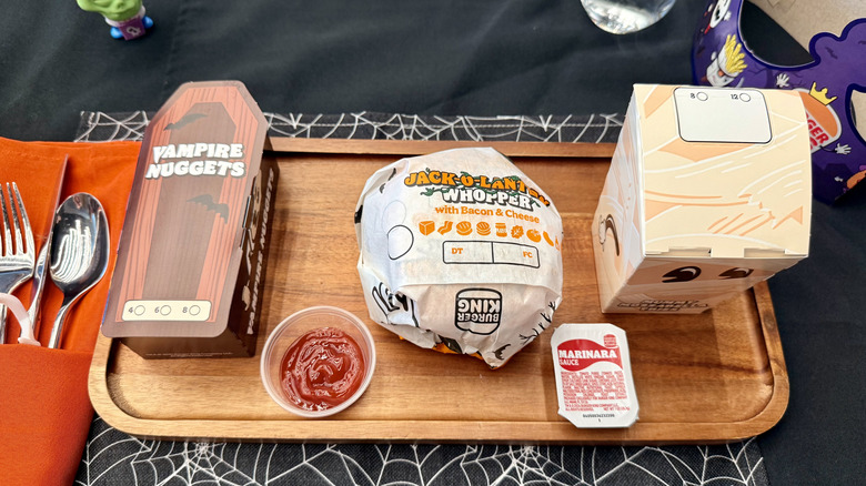 Wrapped menu items from Burger King's Halloween 2025 menu sitting on a wooden platter