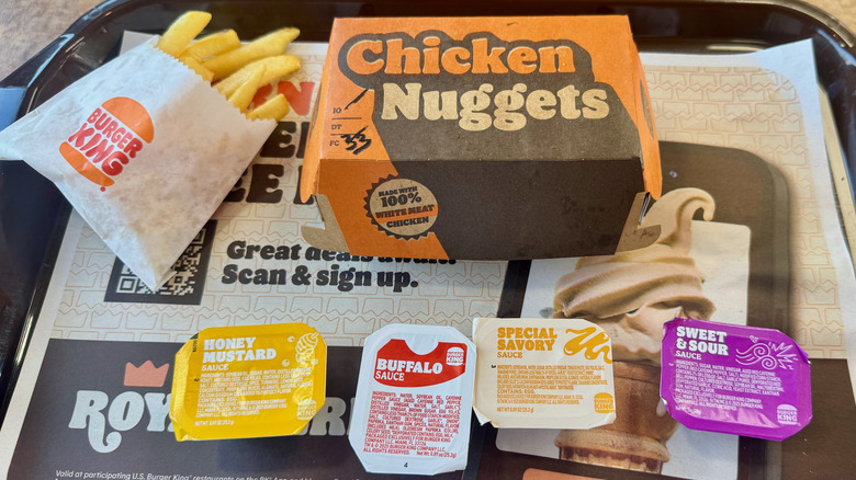 A brown plastic tray with a cardboard box of nuggets, small french fries, and four dipping sauces.