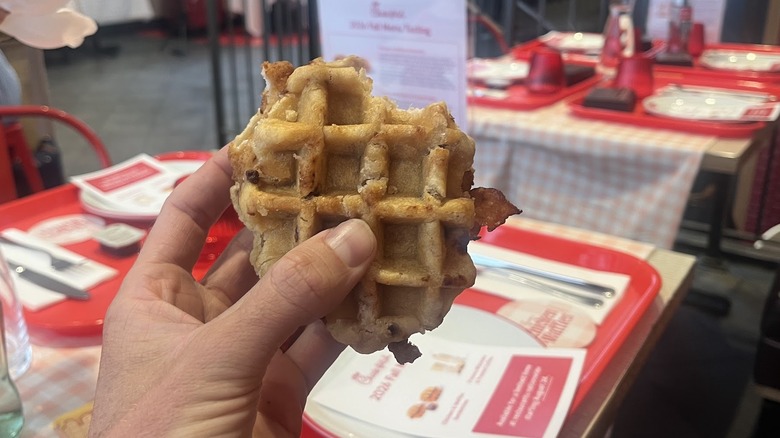 A hand holds a Chick-fil-A Chicken & Waffles Sandwich