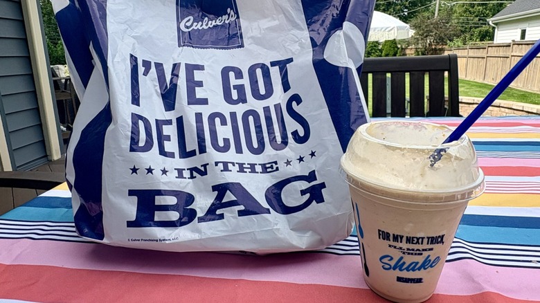 A takeout cup of Culver's Pumpkin S'mores Concrete Mixer on a picnic table next to Culver's takeout bag