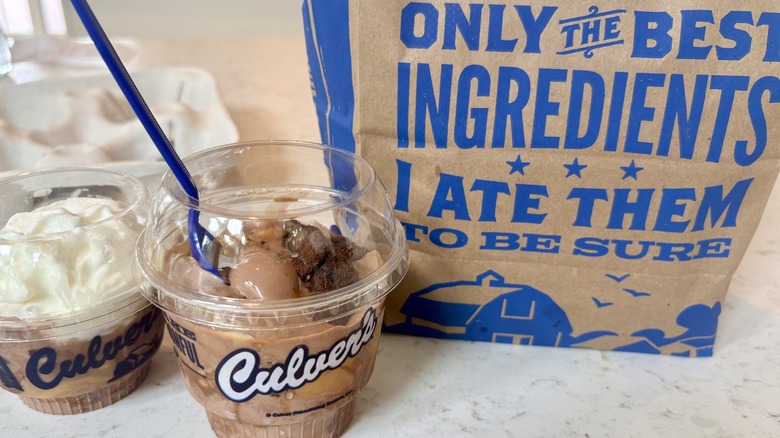 Two takeout dishes of Culver's new Peanut Butter Fudge Brownie flavor of the day next to a takeout bag