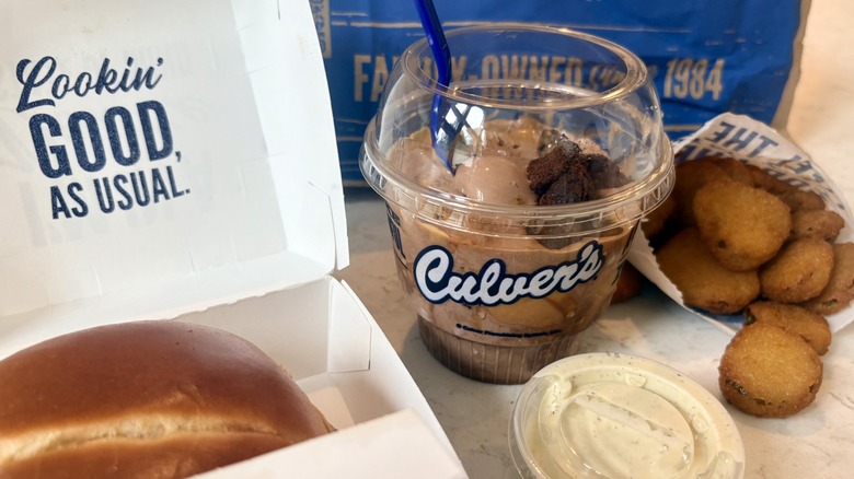 A meal from Culver's with a sandwich, fried pickles, and a takeout dish of peanut butter fudge brownie frozen custard